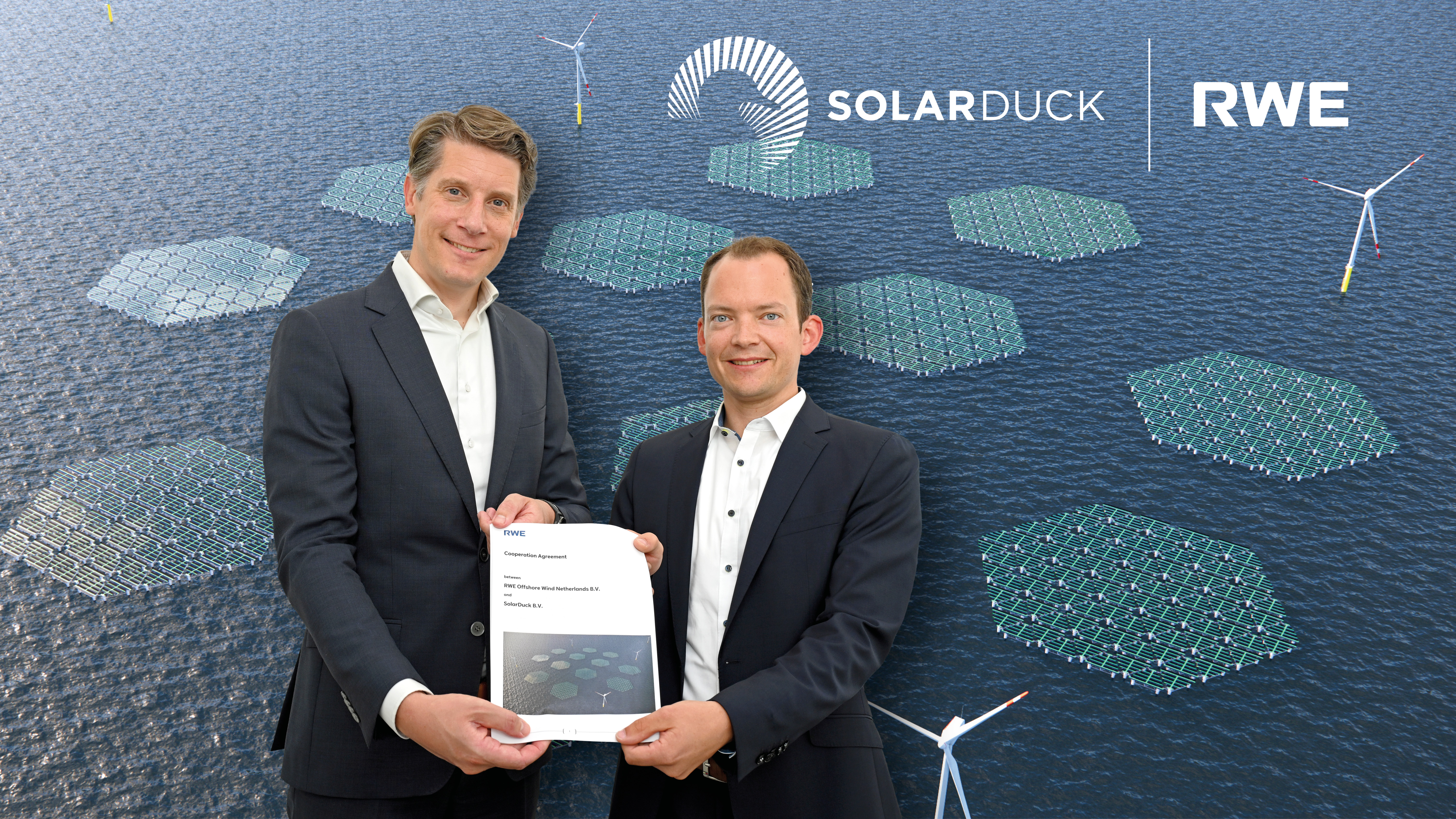 Zwei Fachleute halten eine Kooperationsvereinbarung mit Solarpanelen und Windturbinen im Hintergrund.