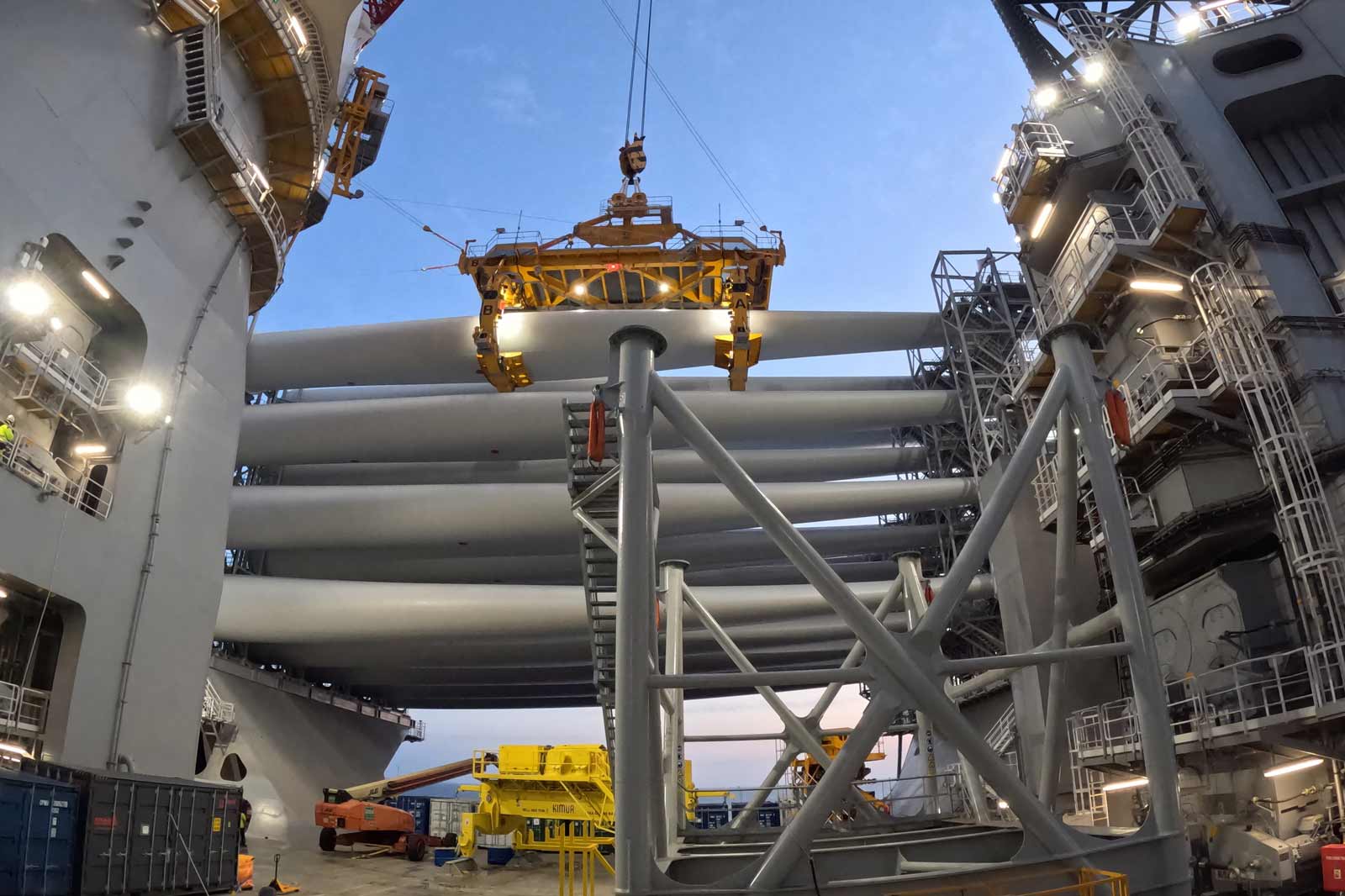 Ein Kran hebt große Rohre auf einer Offshore-Plattform an, umgeben von verschiedenen Maschinen und Beleuchtung.