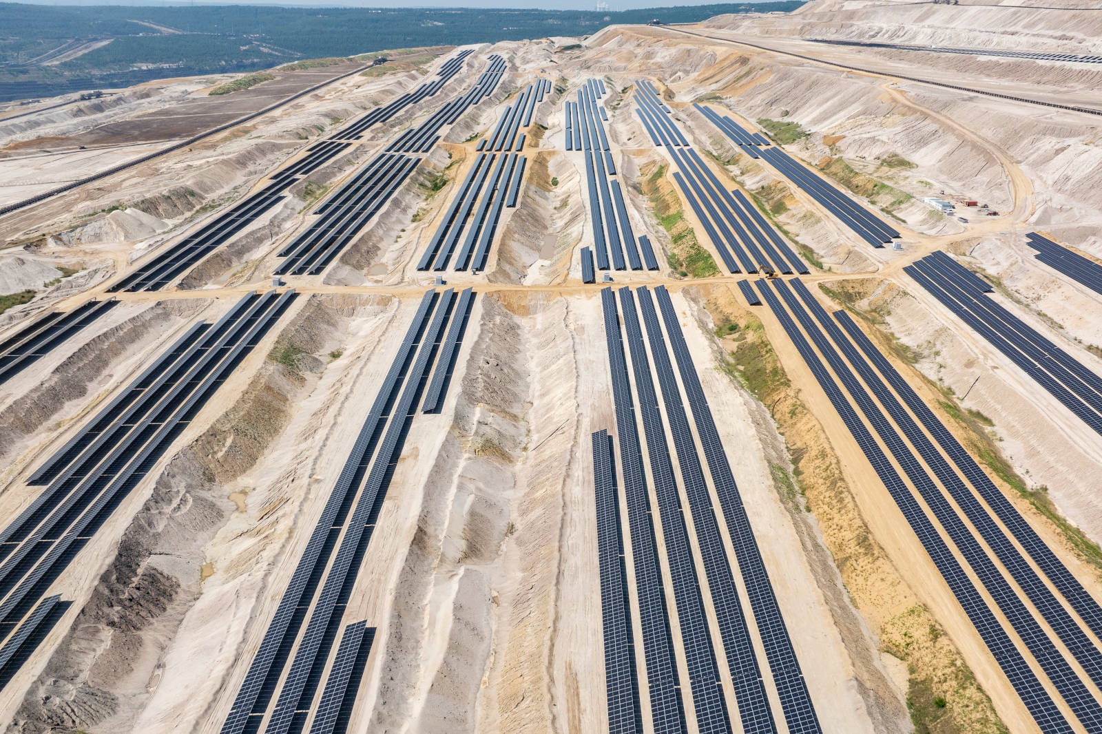 Eine große Solarfarm mit zahlreichen Solarpanelen, die in langen Reihen auf unebenem Gelände angeordnet sind.