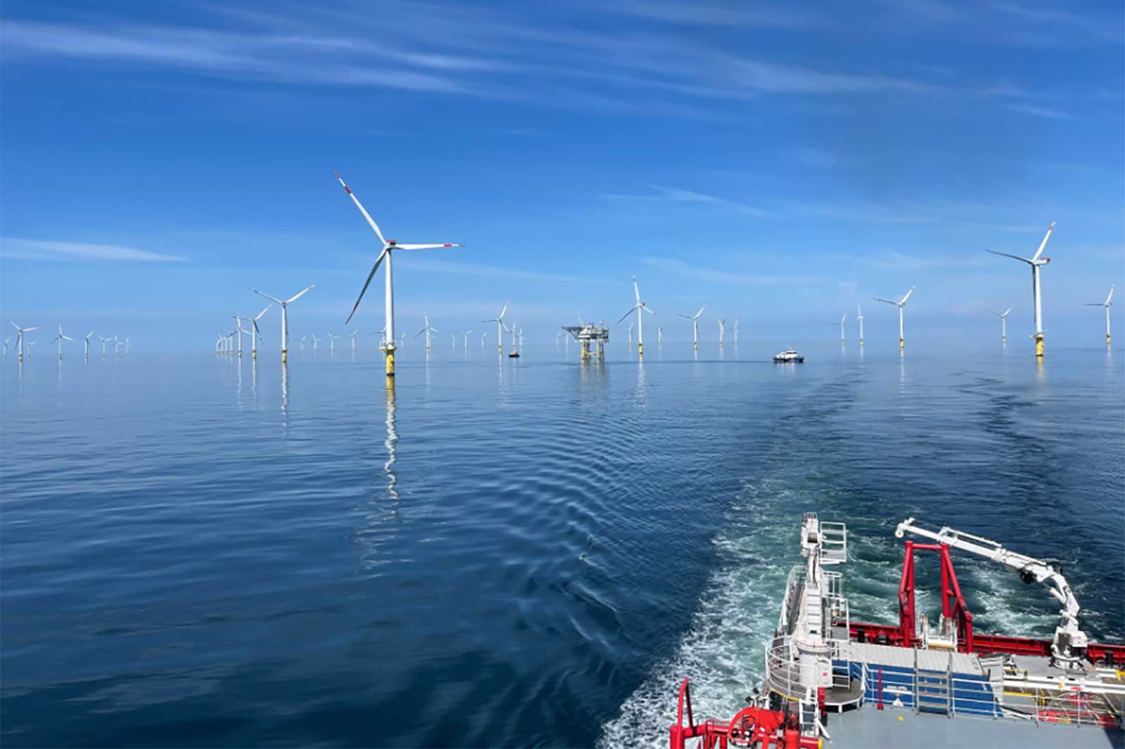 Ein ruhiger Blick auf einen Offshore-Windpark mit vielen Turbinen und ruhigem Wasser, gesehen von einem Boot.