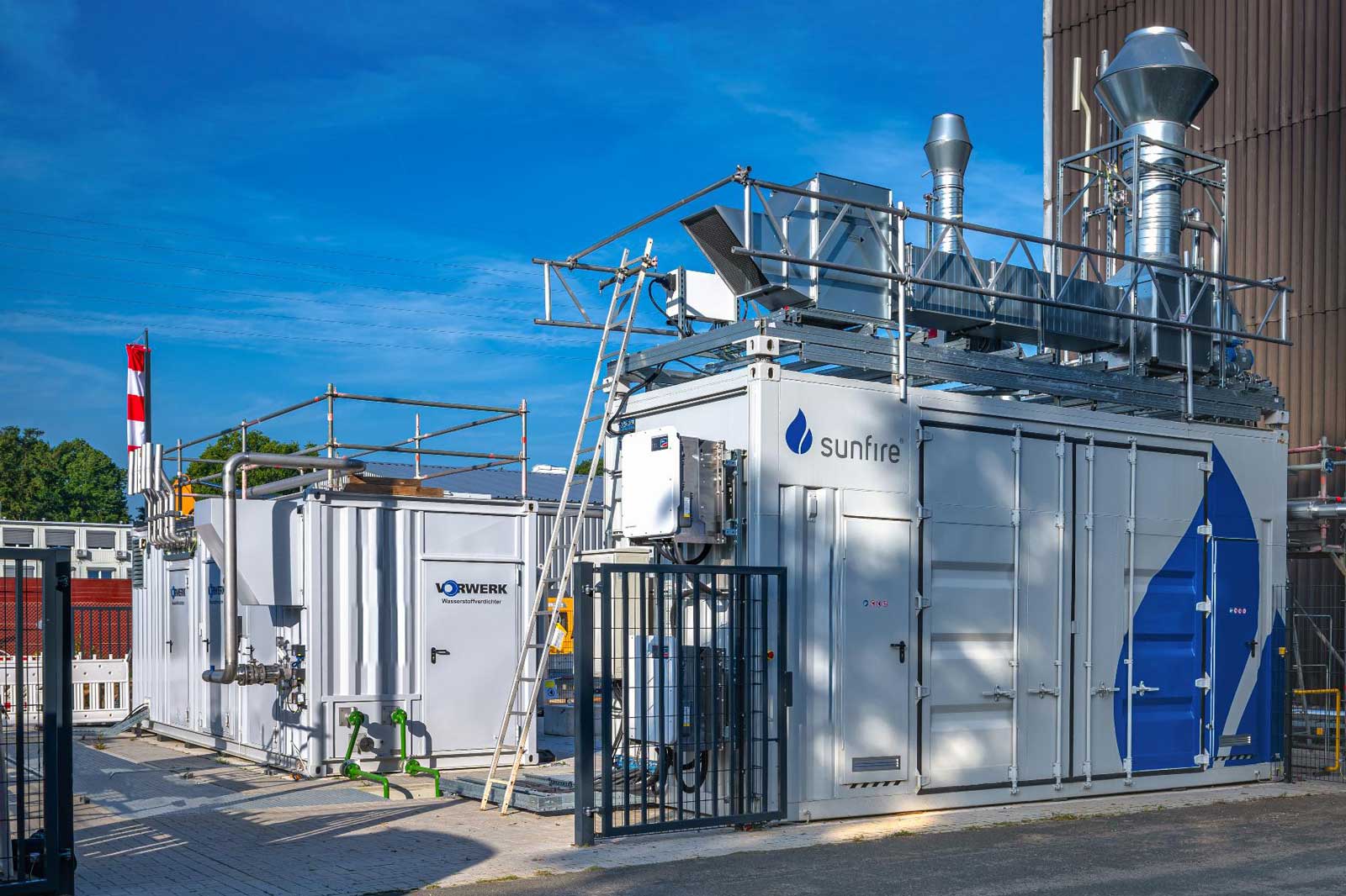 Zwei modulare Energiecontainer mit Ventilen und Rohren. Ein Aufzug und eine Flagge sind sichtbar.