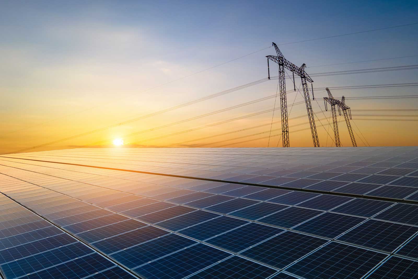Solar panels stretch across the landscape, with power lines silhouetted against a vibrant sunset sky.