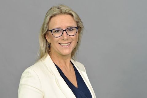 Eine Frau mit langen, blonden Haaren trägt einen Blazer über einem marineblauen Oberteil vor einem grauen Hintergrund. Portrait von Federica Maranca.