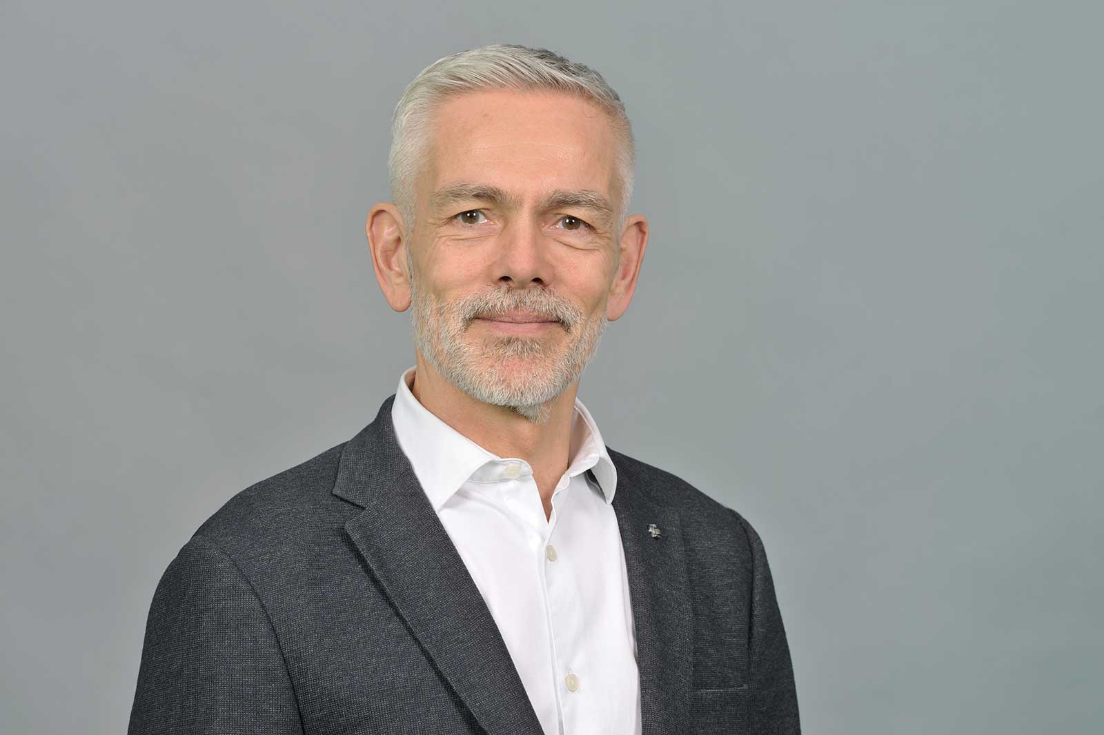 Ein Mann in einem grauen Anzug und einem weißen Hemd steht vor einem grauen Hintergrund. Portrait von Gareth Cribb.