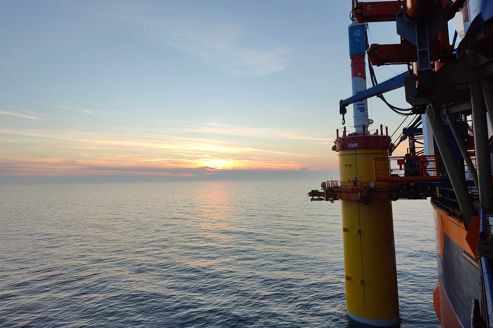 Ein lebendiger Sonnenuntergang über ruhigem Meerwasser mit einer Offshore-Plattform im Vordergrund.