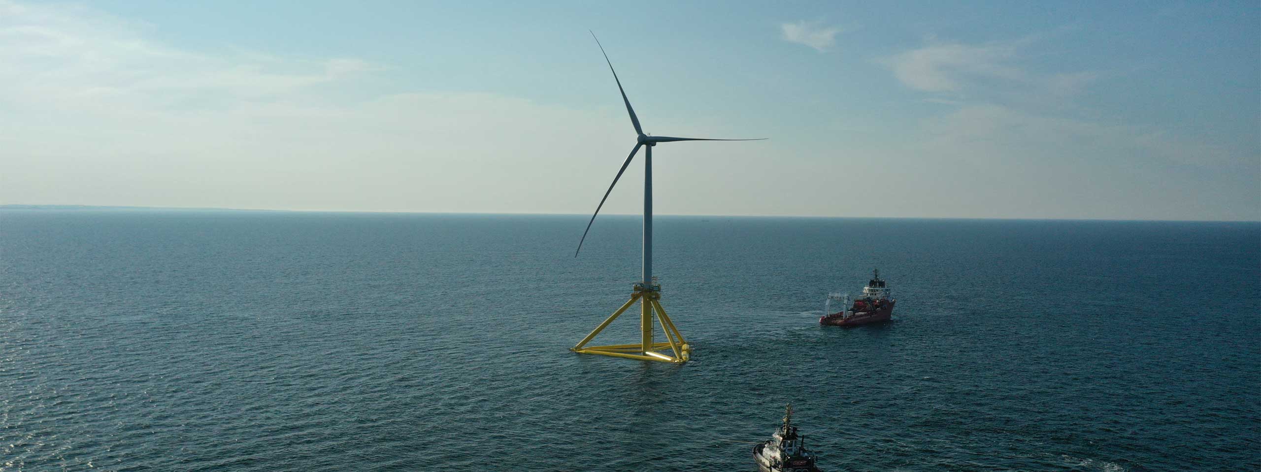 Ein einzelner Offshore-Windkraftanlage steht im Wasser, umgeben von sanften Wellen, mit einem Schiff im Hintergrund.