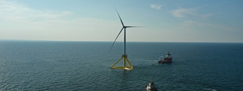 Ein einzelner Offshore-Windkraftanlage steht im Wasser, umgeben von sanften Wellen, mit einem Schiff im Hintergrund.