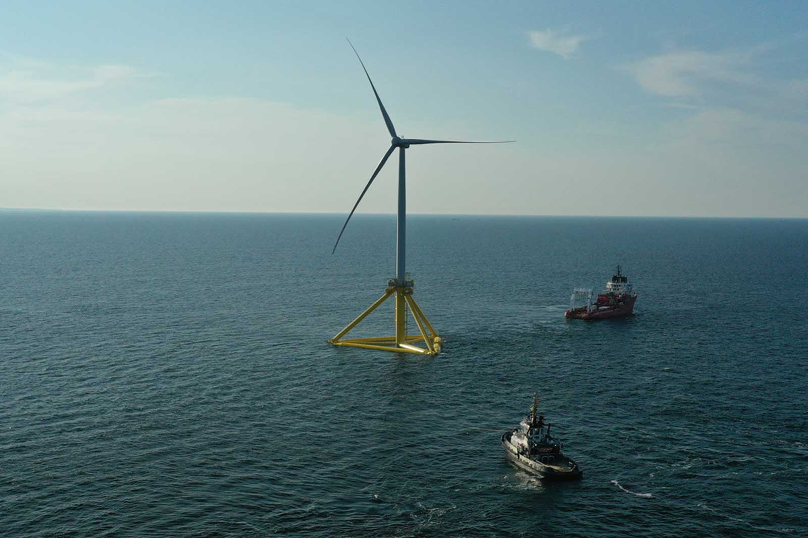Ein Offshore-Windrad steht in der See, während ein Schiff in der Nähe fährt.