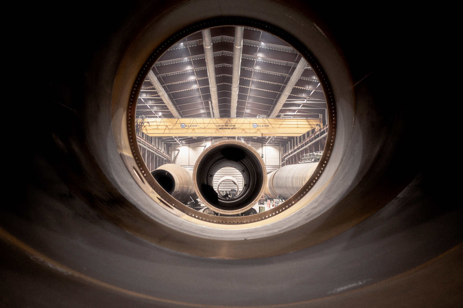Blick durch große Rohre in einer Industriehalle mit einem Kran im Hintergrund und weiteren Rohren im Raum.