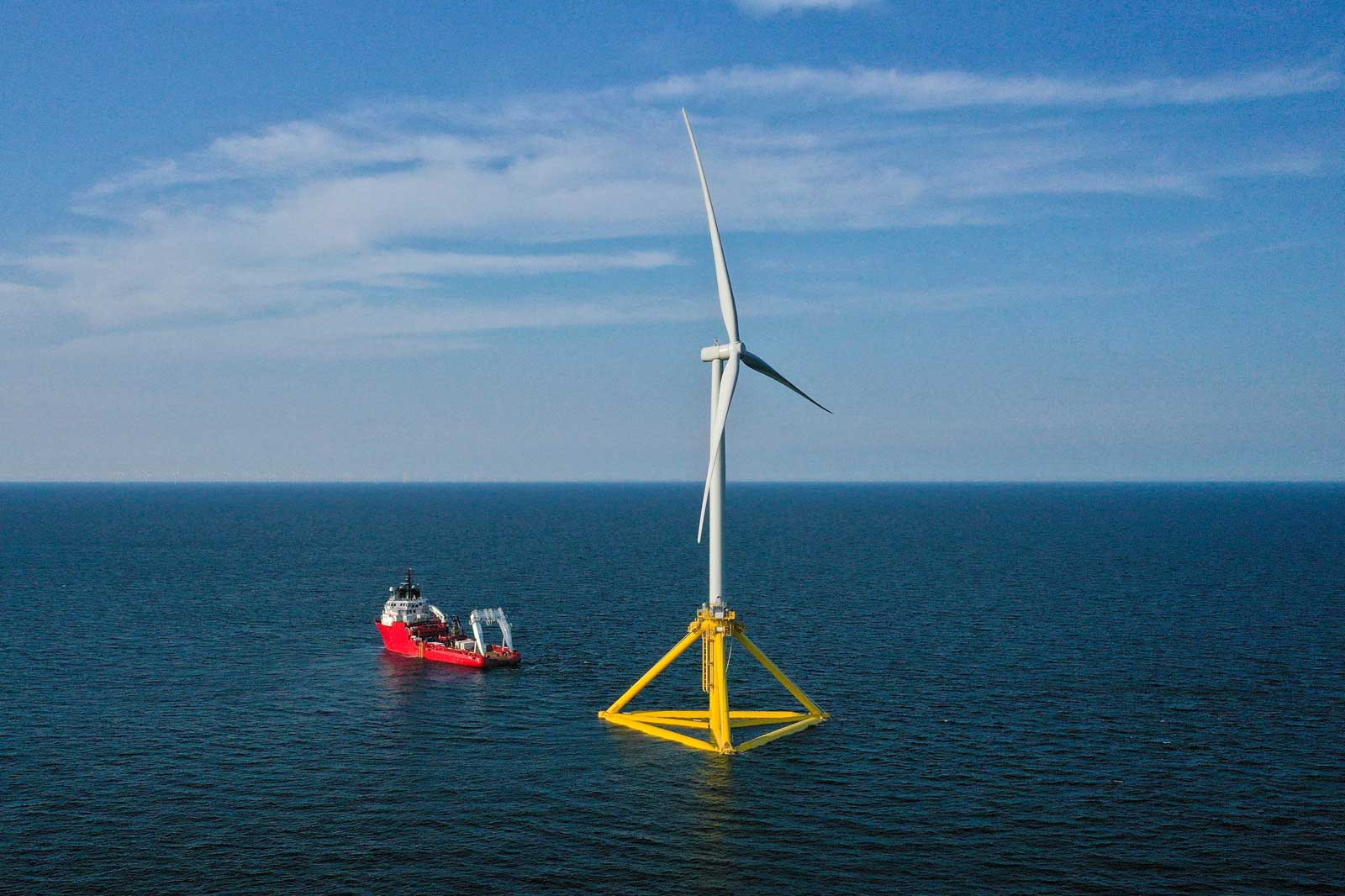 Ein Windkraftwerk steht in der Ostsee, während ein Schiff in der Nähe fährt. Der Himmel ist blau mit wenigen Wolken.