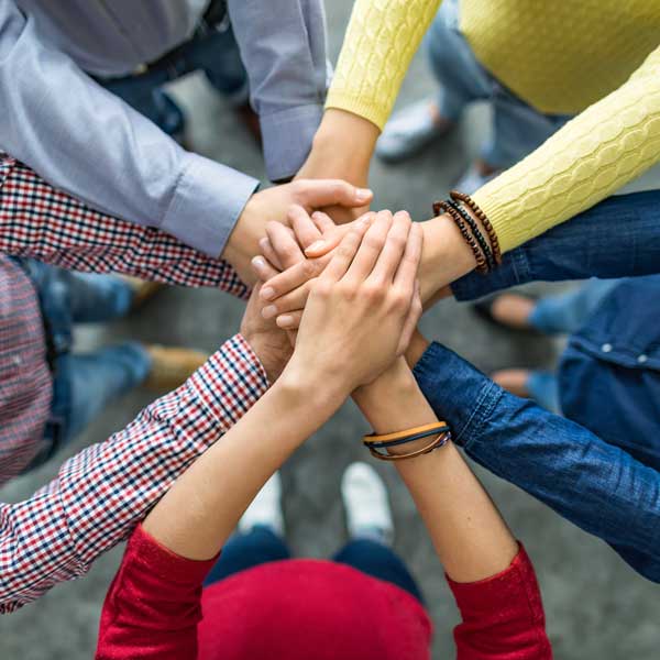 Hände von mehreren Personen, die sich in der Mitte treffen, symbolisieren Zusammenarbeit und Teamgeist.