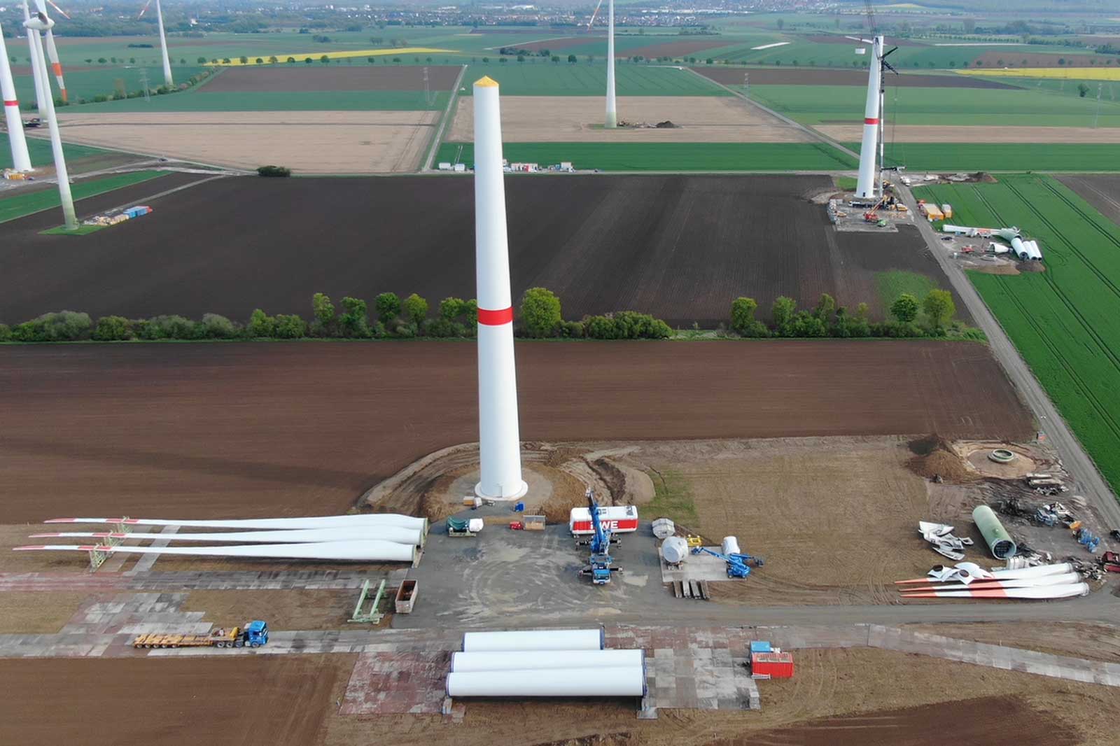 Ein Windkraftanlagenstandort mit mehreren Windturbinen, Blättern und Baugeräten auf einem grünen Feld.