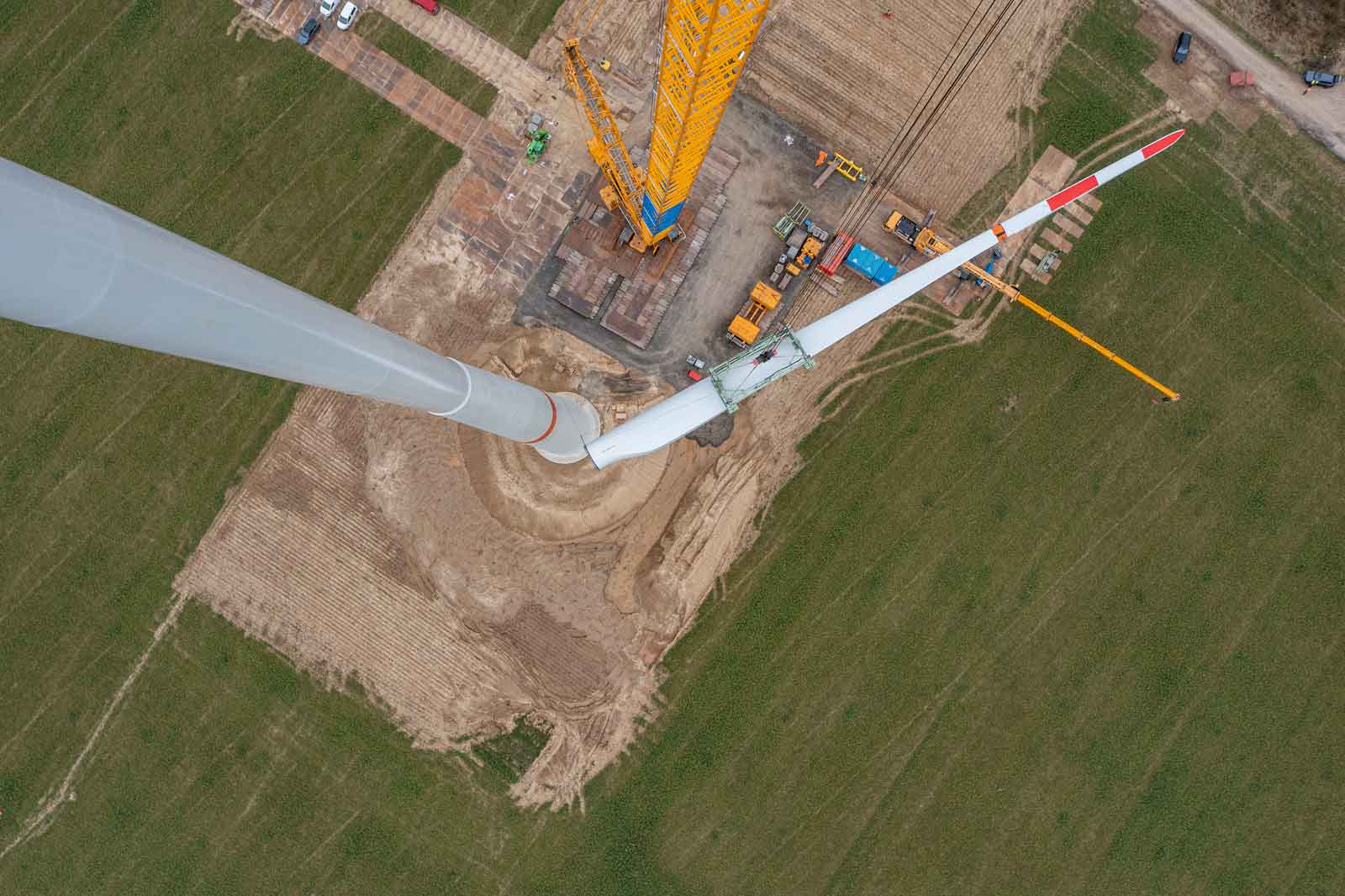 Ein Blick auf einen Windkraftanlagen-Bauplatz aus der Vogelperspektive mit einem Kran und einem Turbinenteil.