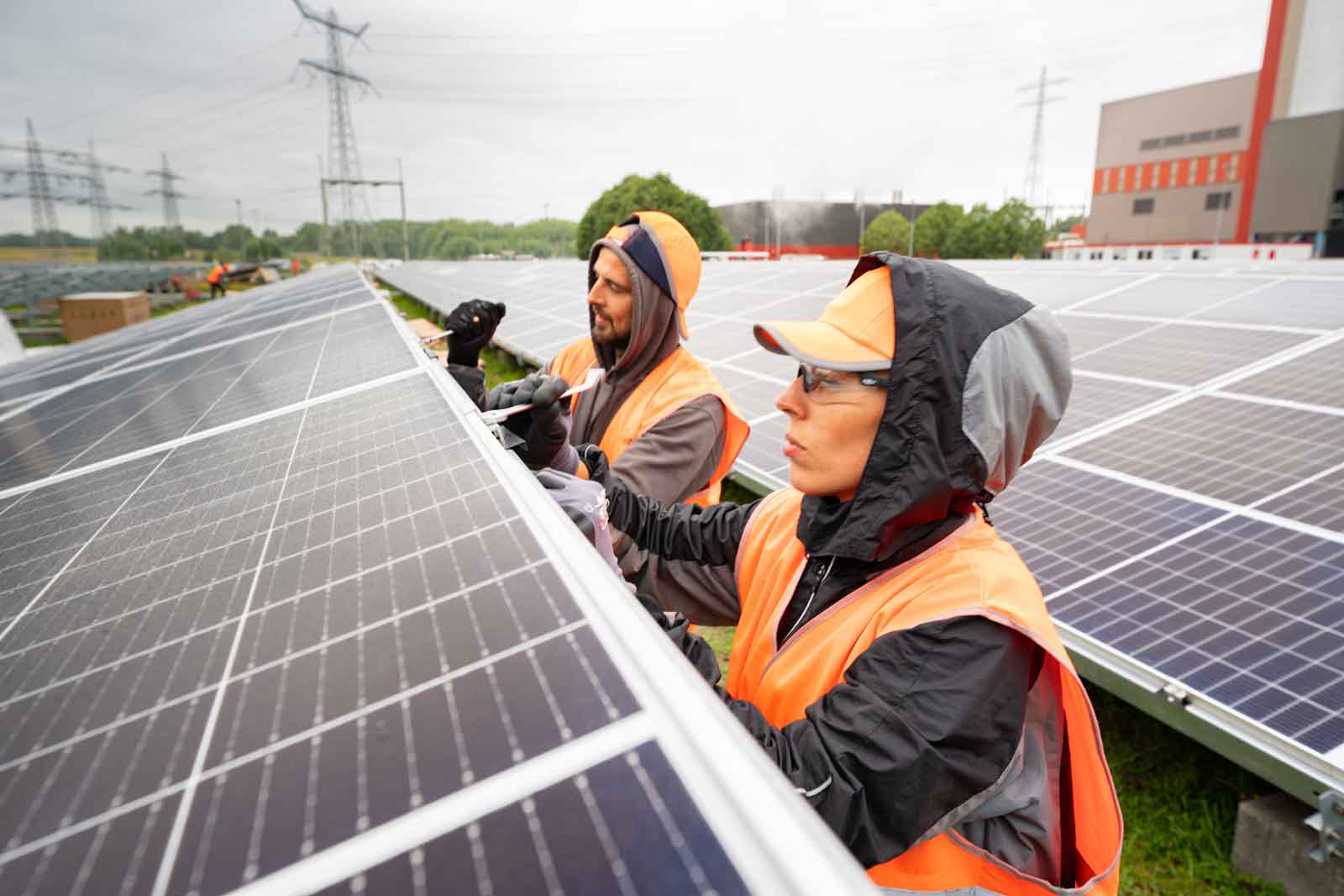 Arbeiter montieren Solarpanels auf einer großen Solarfarm, umgeben von weiteren Panels und Strommasten.