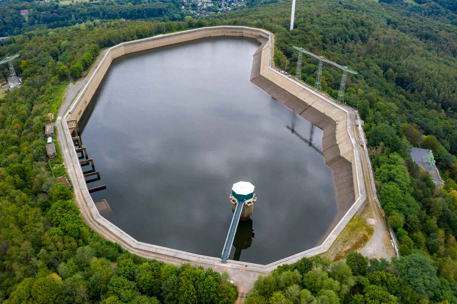 Luftaufnahme eines Wasserspeichers, umgeben von Bäumen und einer Betonmauer, die den Wasserstand beaufsichtigt.