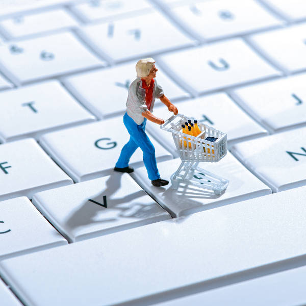 A small figure with a shopping cart stands on a computer keyboard, transporting bottles.