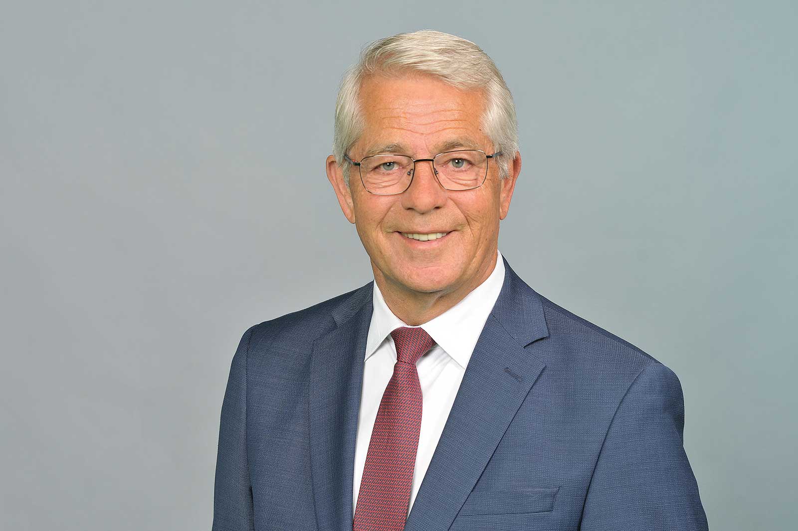 A professionally dressed man stands by a railing in a modern setting. Portrait of Dr. Stefan Schulte.