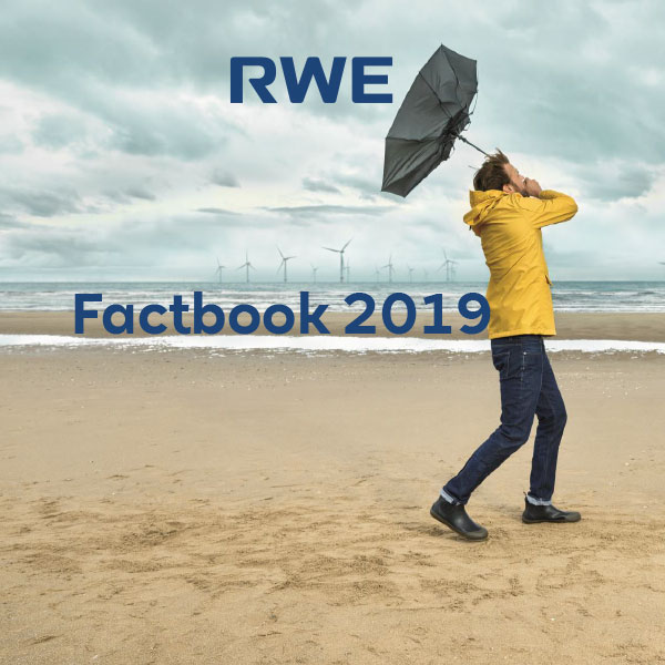 Eine Person in einer gelben Regenjacke hält einen Regenschirm am Strand, mit Windkraftanlagen im Hintergrund.
