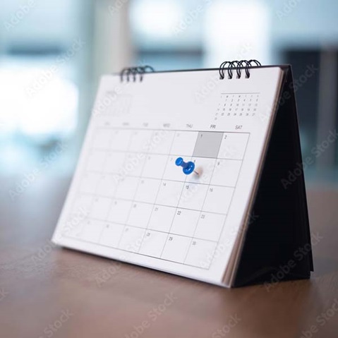Ein Tischkalender mit einem blauen Pinnnadel, der auf ein bestimmtes Datum zeigt, steht auf einem Tisch.