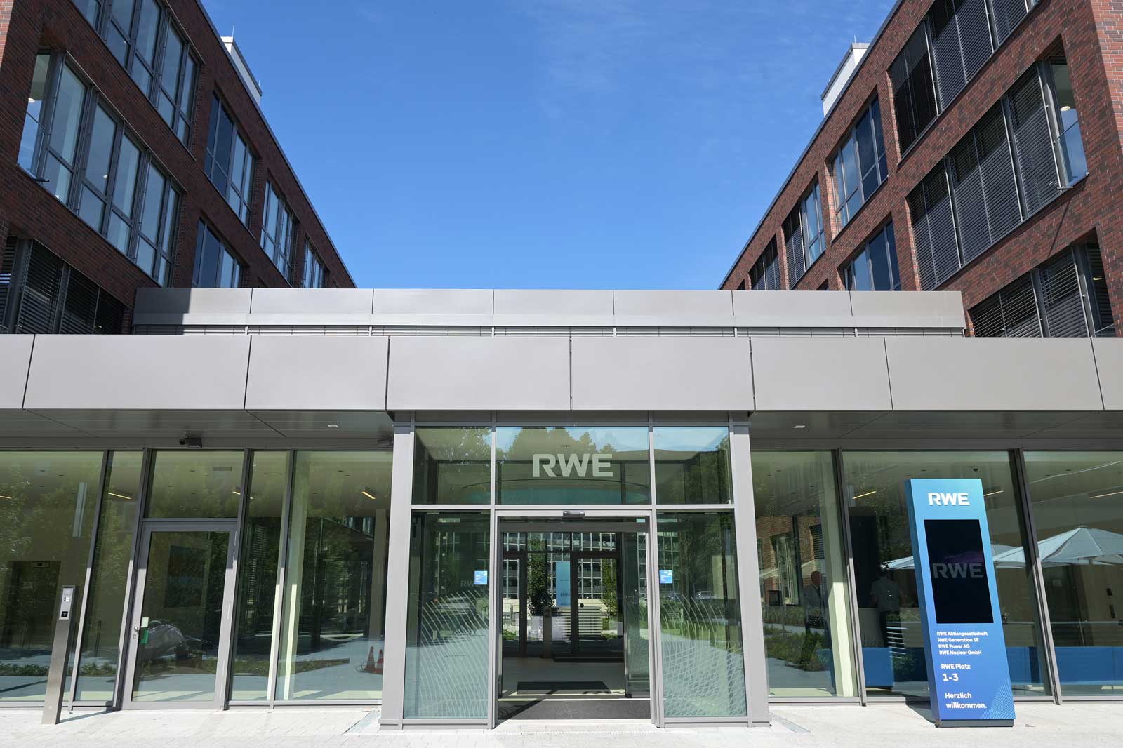Moderne Eingangsfront eines RWE-Gebäudes mit großen Fenstern und Informationssäule im Freien.