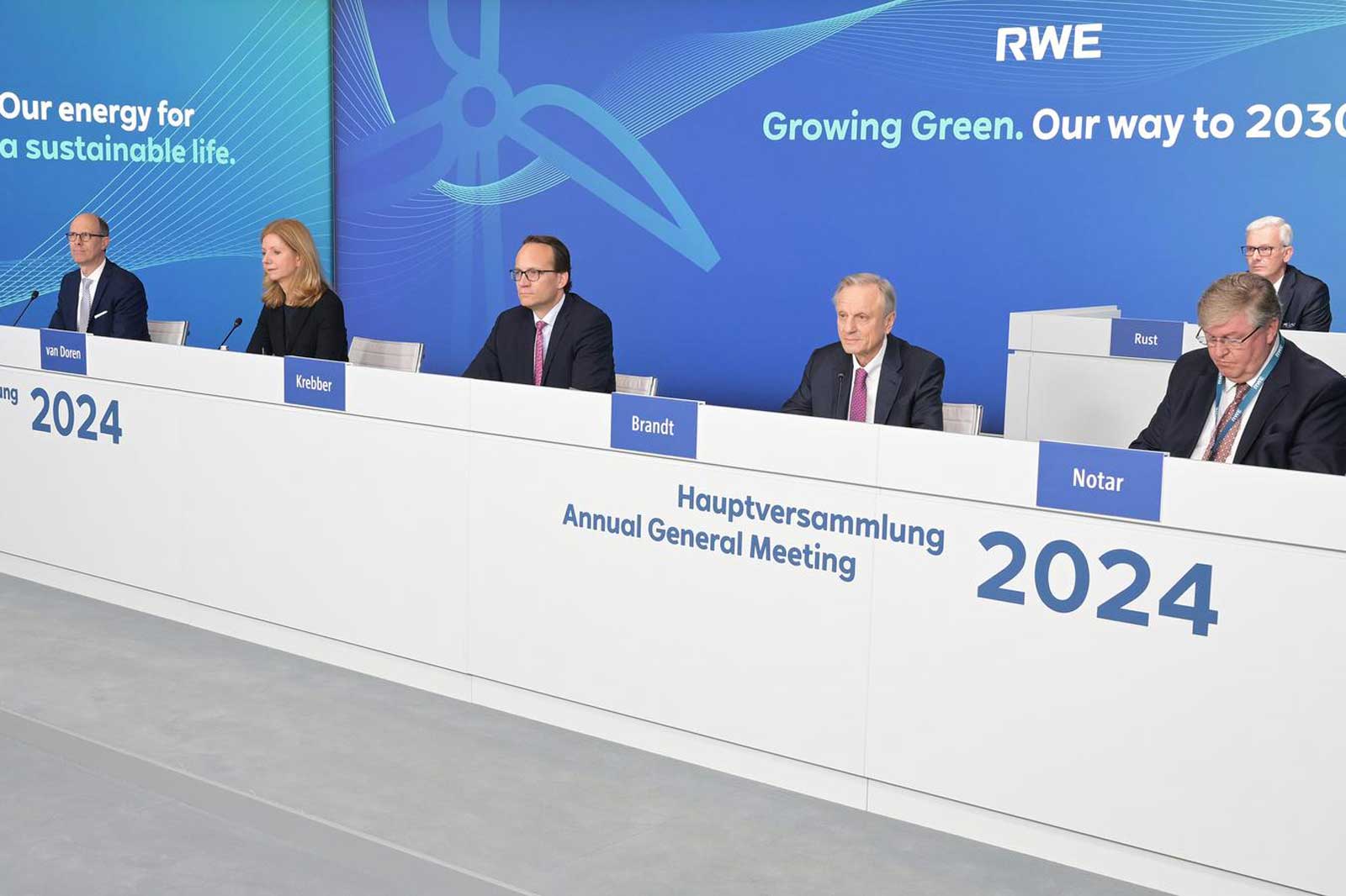 Eine Gruppe von Personen sitzt an einem Tisch während der Hauptversammlung 2024 von RWE. Hinter ihnen steht das Unternehmenslogo.
