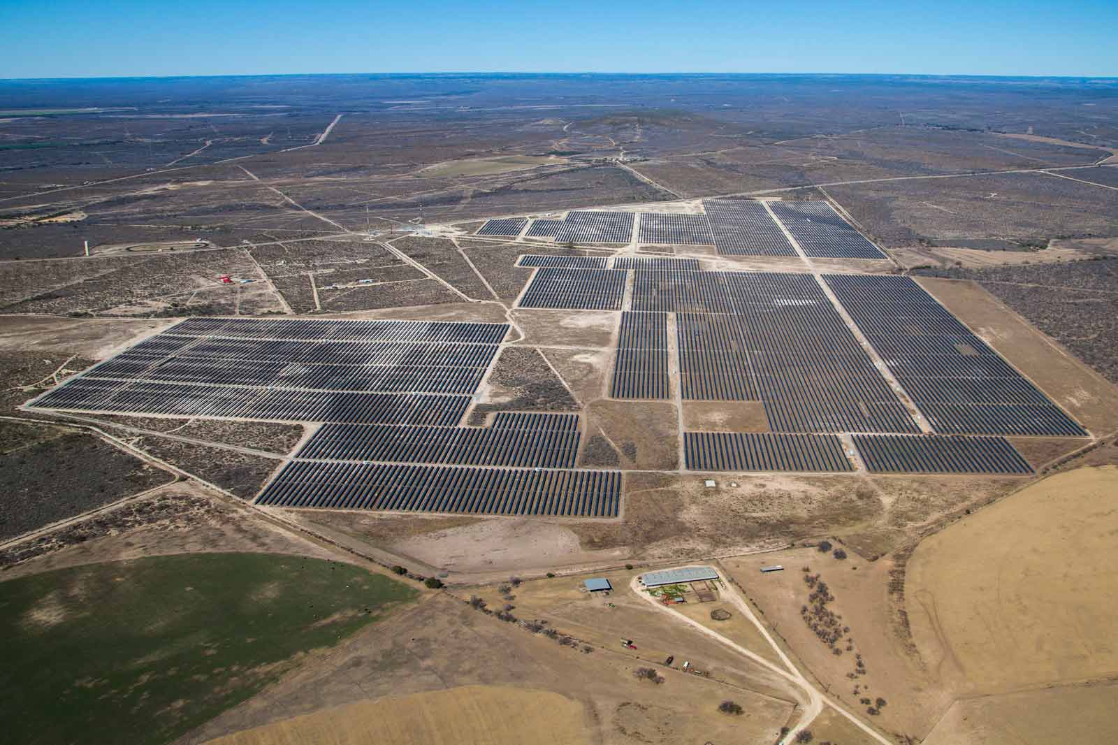 Eine große Solaranlage erstreckt sich über eine weitläufige Landschaft mit mehreren Solarpanelen und weiten Feldern im Hintergrund.