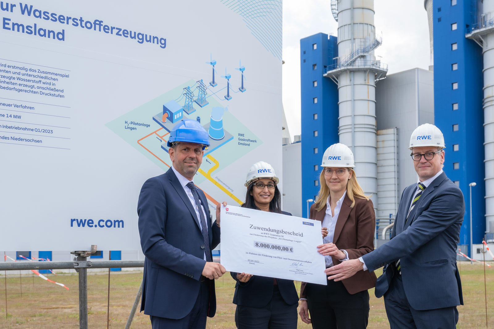 Gruppenfoto vor einem Banner zur Wasserstofferzeugung, eine Gruppe hält einen großen Scheck über 8 Millionen Euro.