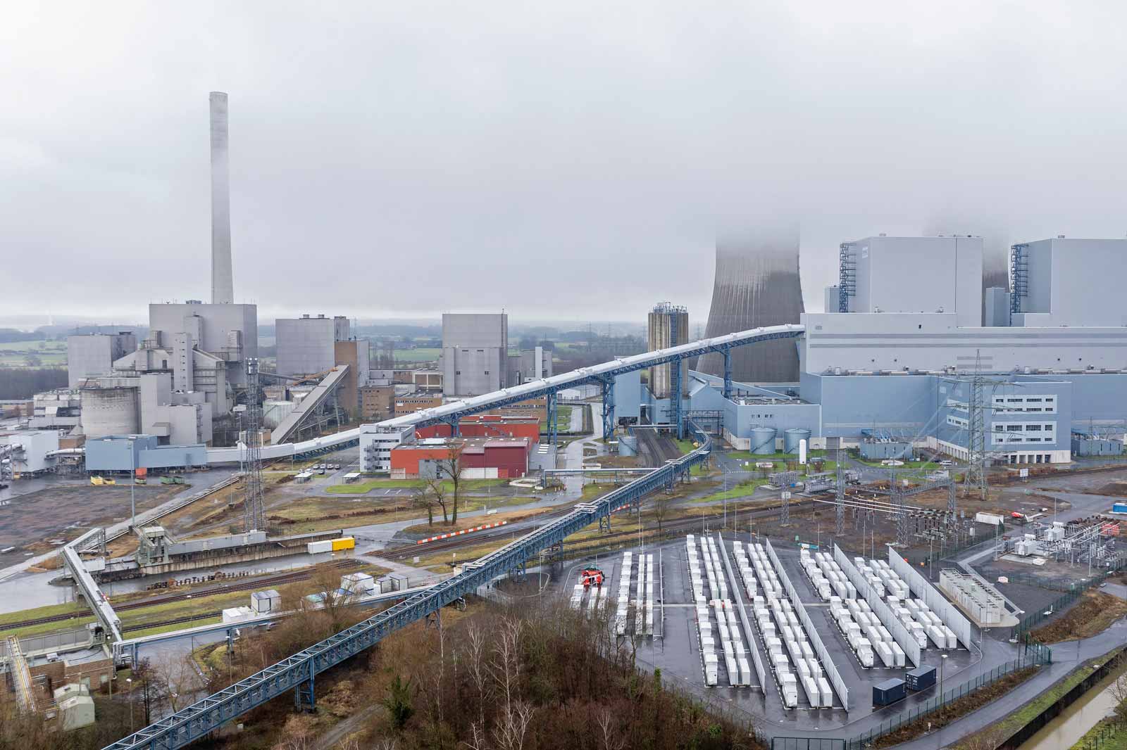 Eine Panoramaansicht eines Industriekomplexes mit Lagerhäusern, Förderbändern und einem hohen Schornstein, der im Nebel gehüllt ist.