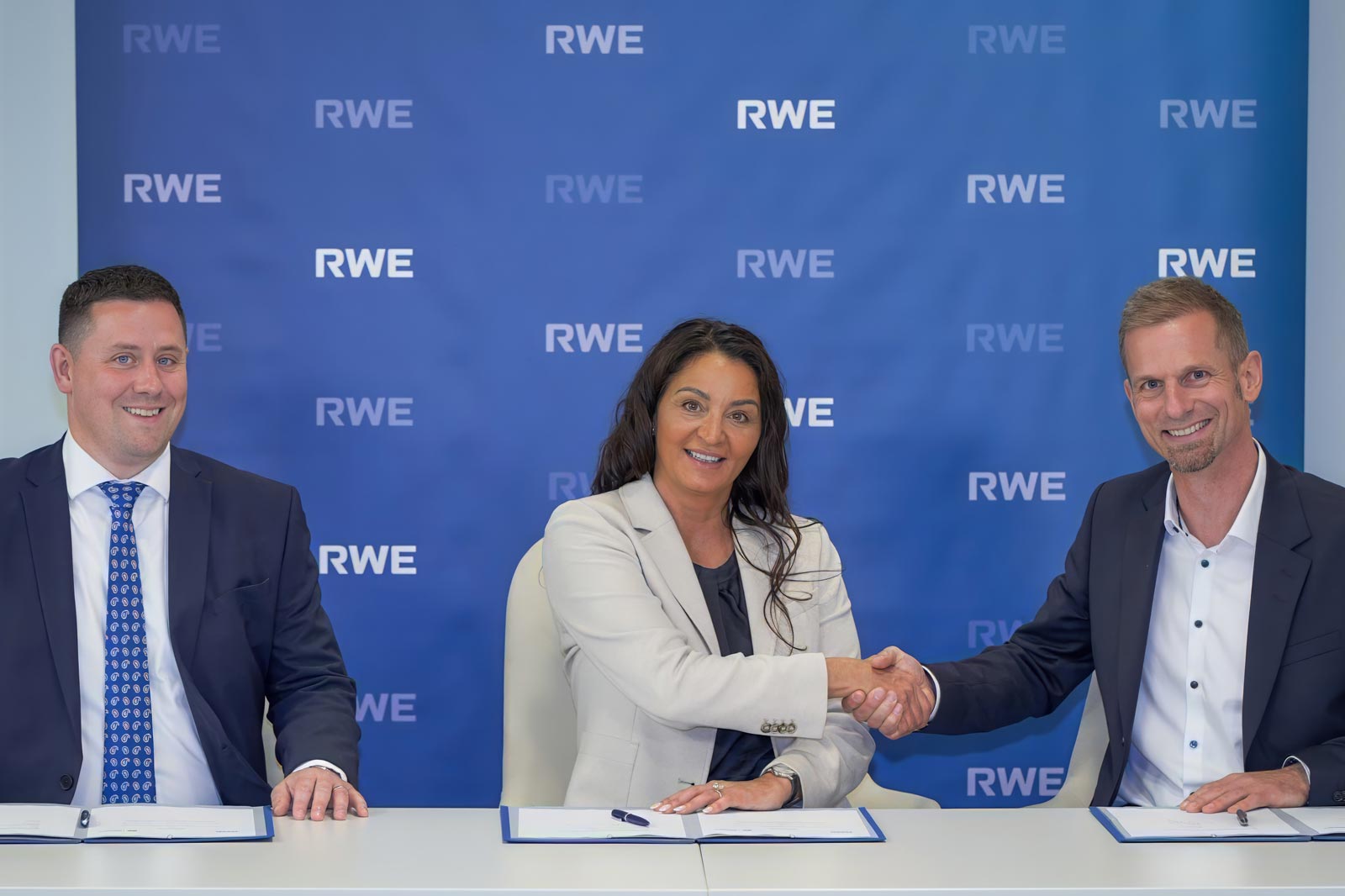 Drei Fachleute bei einer Unterzeichnungsfeier, die sich die Hände schütteln, mit RWE-Logo im Hintergrund.