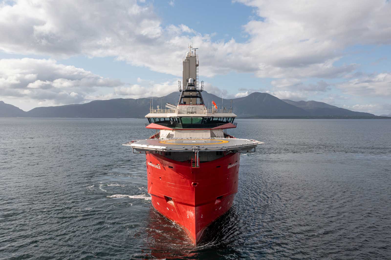 Ein rotes Schiff namens Gran Eagle fährt auf ruhigen Gewässern mit Bergen im Hintergrund und teilweise bewölktem Himmel.