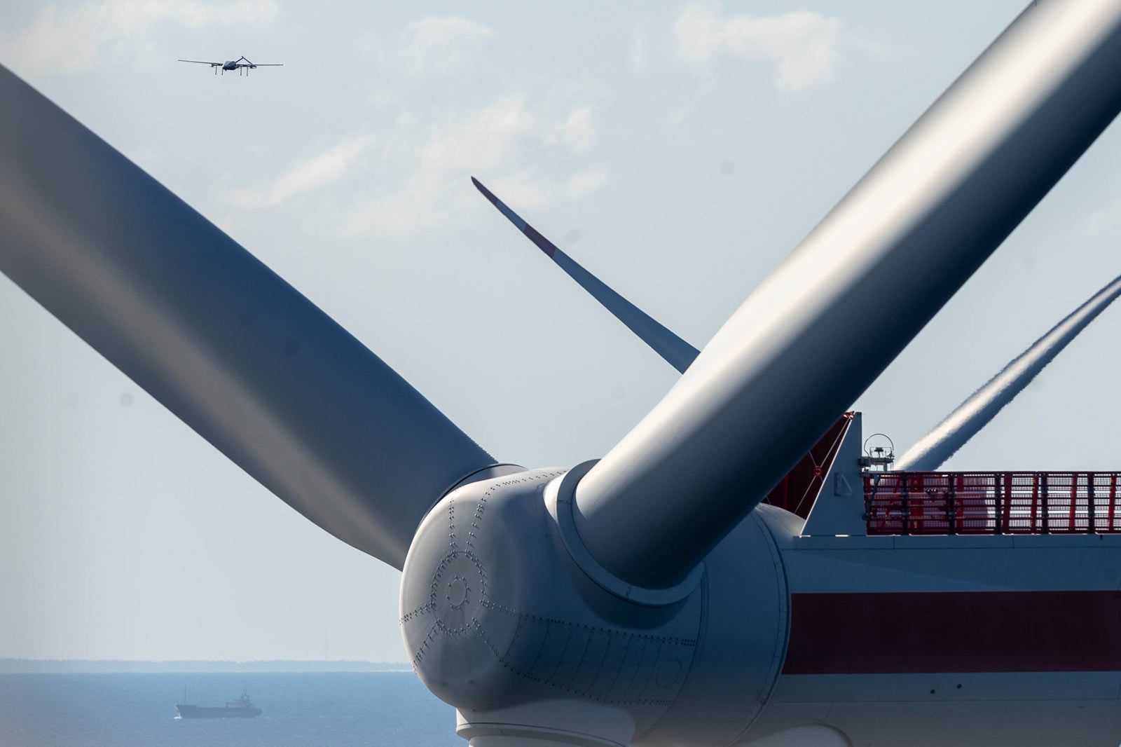 Ein Windrad mit einem großen Rotormesser im Vordergrund und einem Flugzeug, das in der Ferne schwebt.
