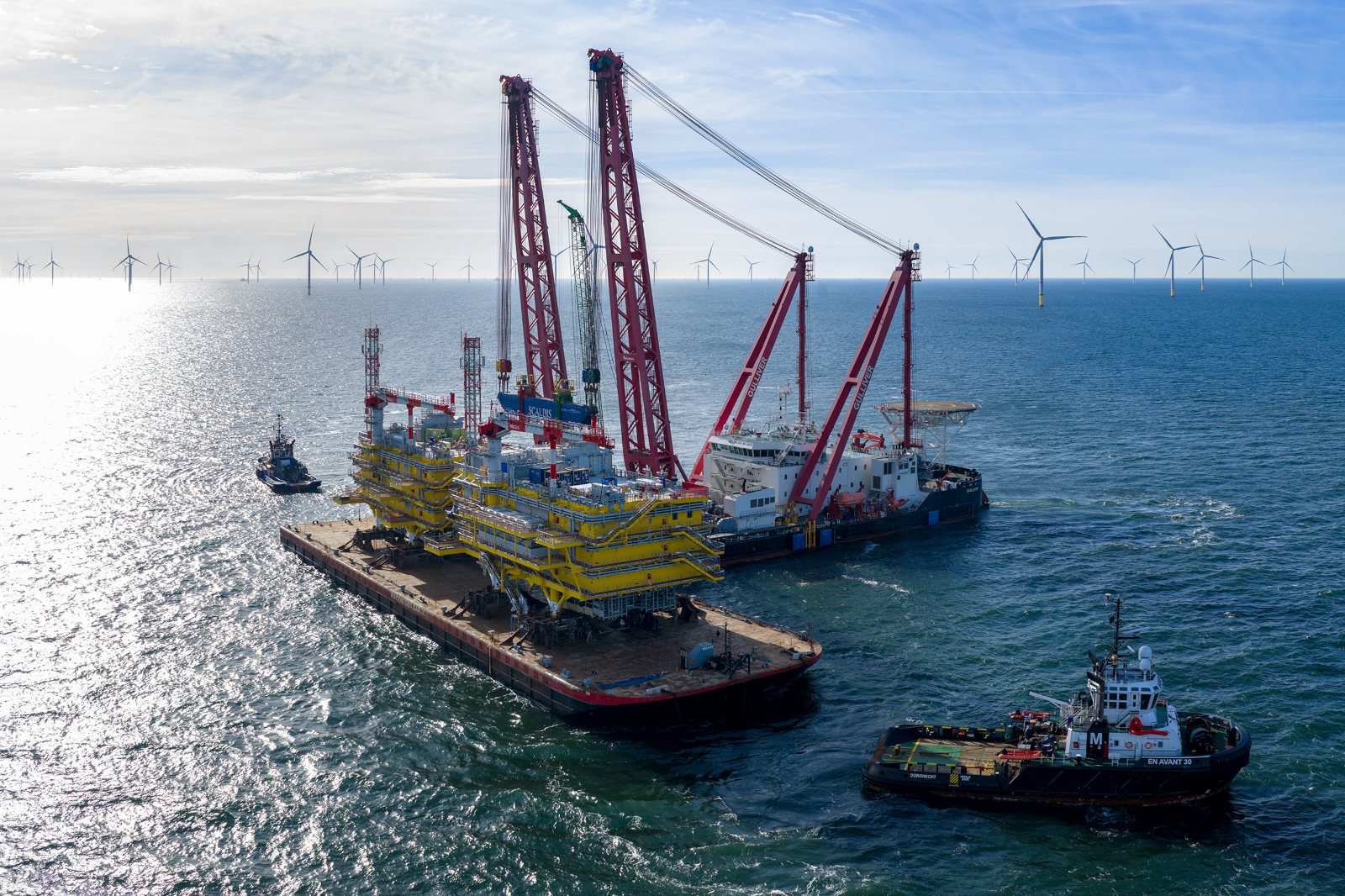 Heavy lift vessel transporting yellow offshore platform modules with tugboats.