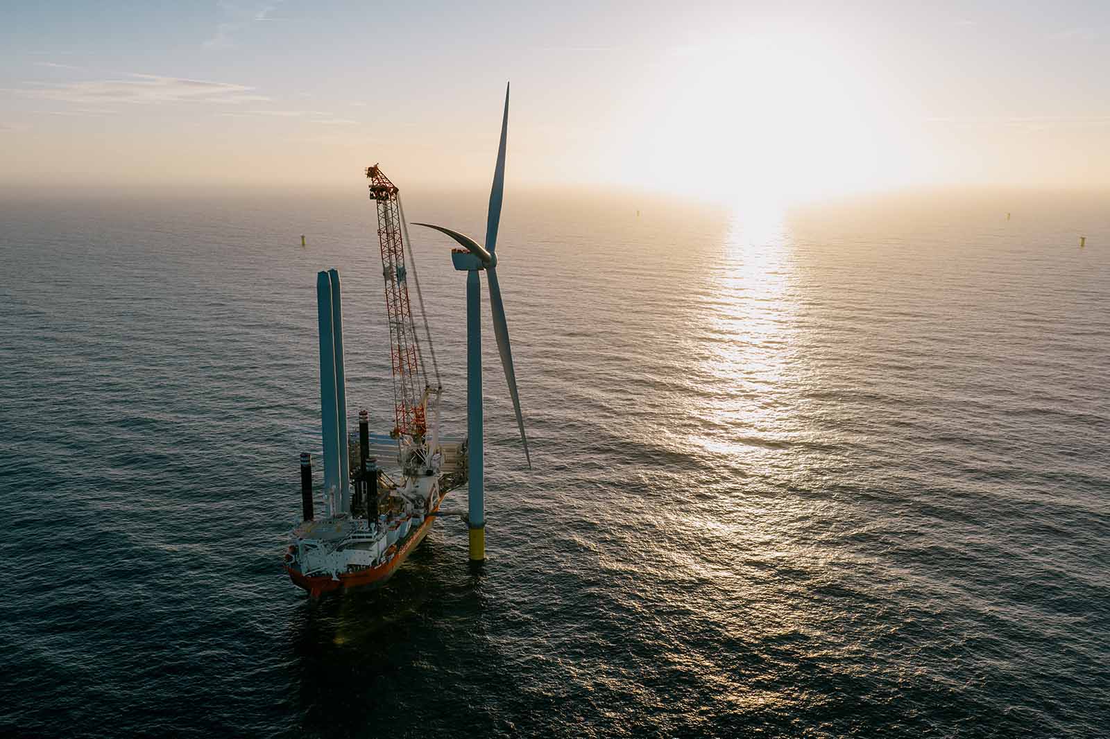 Offshore-Windkraftanlage mit Versorgungsschiff und Kran bei Sonnenuntergang