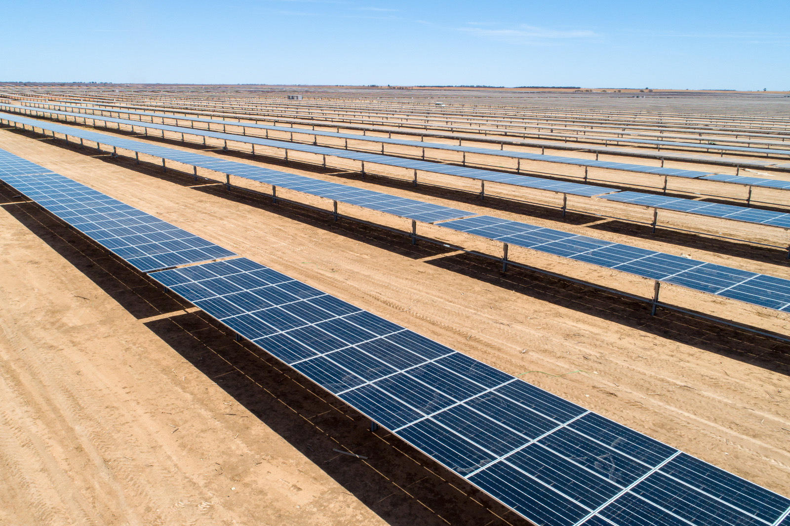 Ein Solarkraftwerk mit umfangreichen Reihen von Solarpanelen auf einer sandigen Landschaft unter einem klaren blauen Himmel.