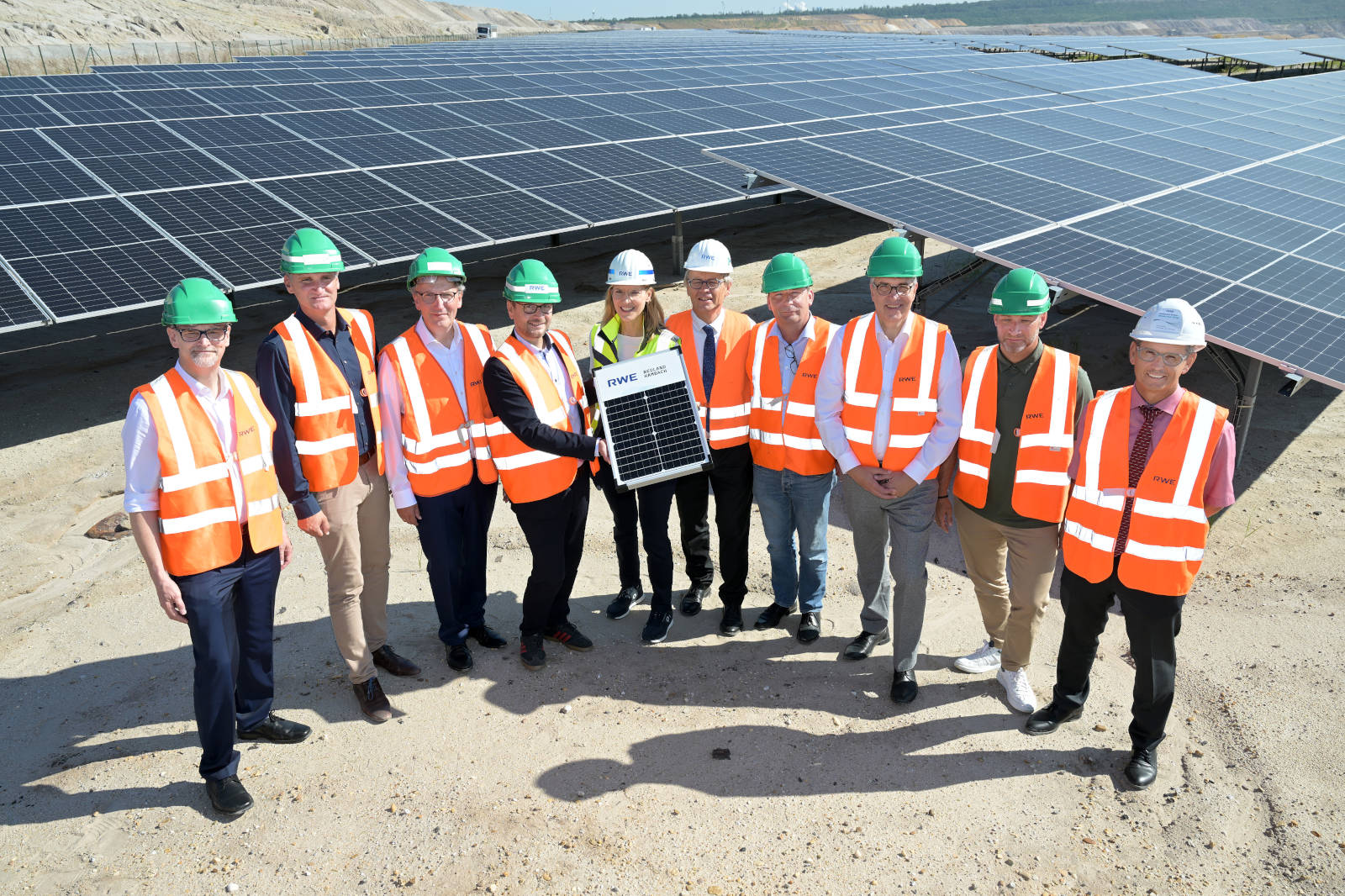 Eine Gruppe von Personen in Sicherheitswesten und Helmen steht in der Nähe von Solarpanelen und hält ein Solarpanel.