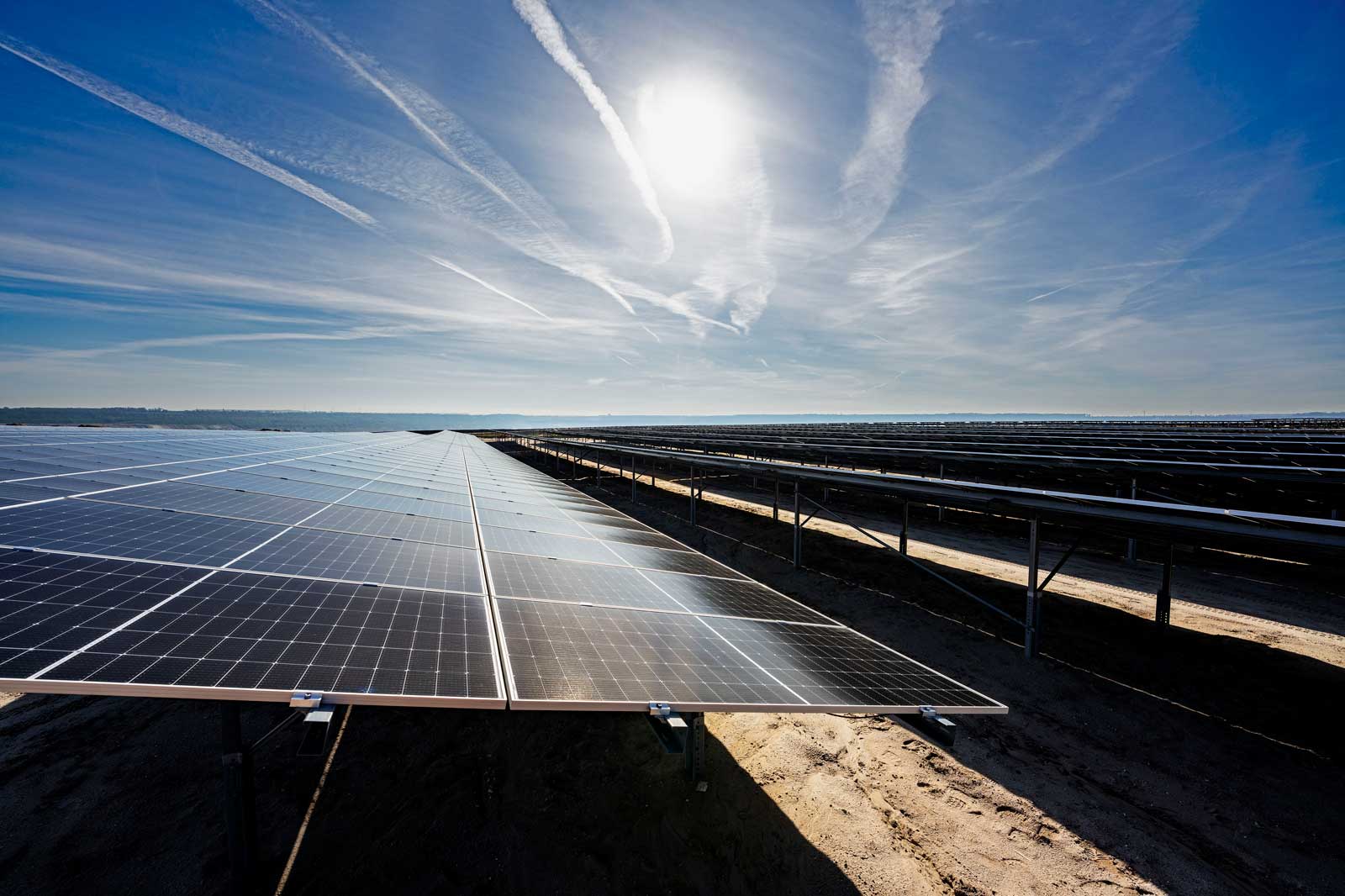 Eine große Solarpark-Anlage mit vielen Solarpanelen, die unter einem klaren Himmel mit Sonnenstrahlen stehen.