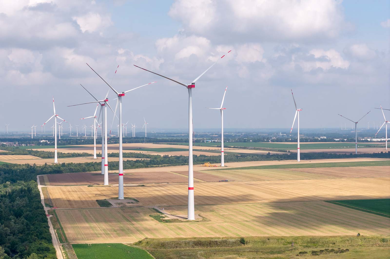 Luftaufnahme von Windkraftanlagen in einer weiten Landschaft mit grünen Feldern und einem bewölkten Himmel.