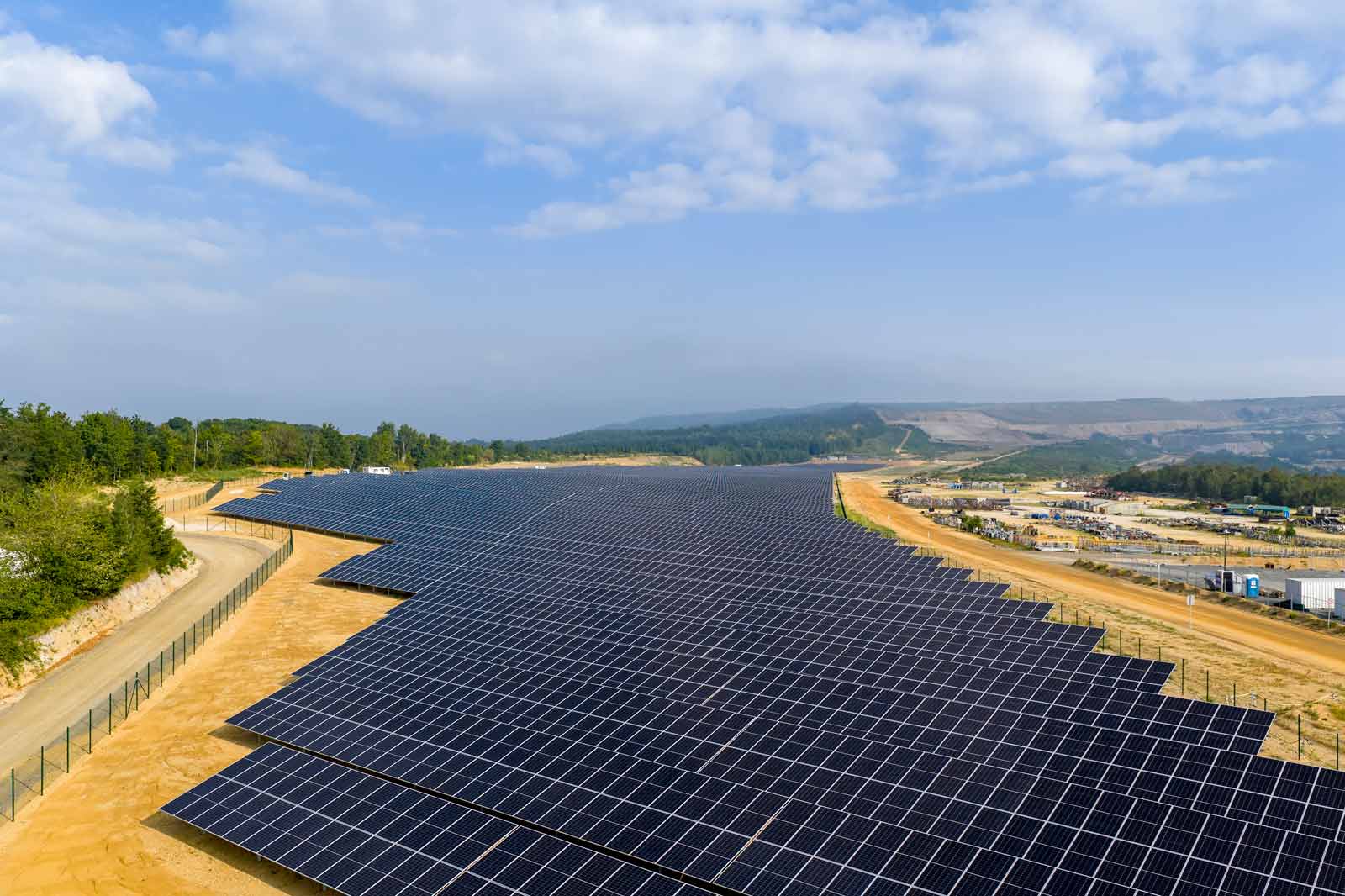Ein großer Solarpark mit vielen Solarpanelen erstreckt sich über ein Gelände unter blauem Himmel und leicht bewölktem Himmel.