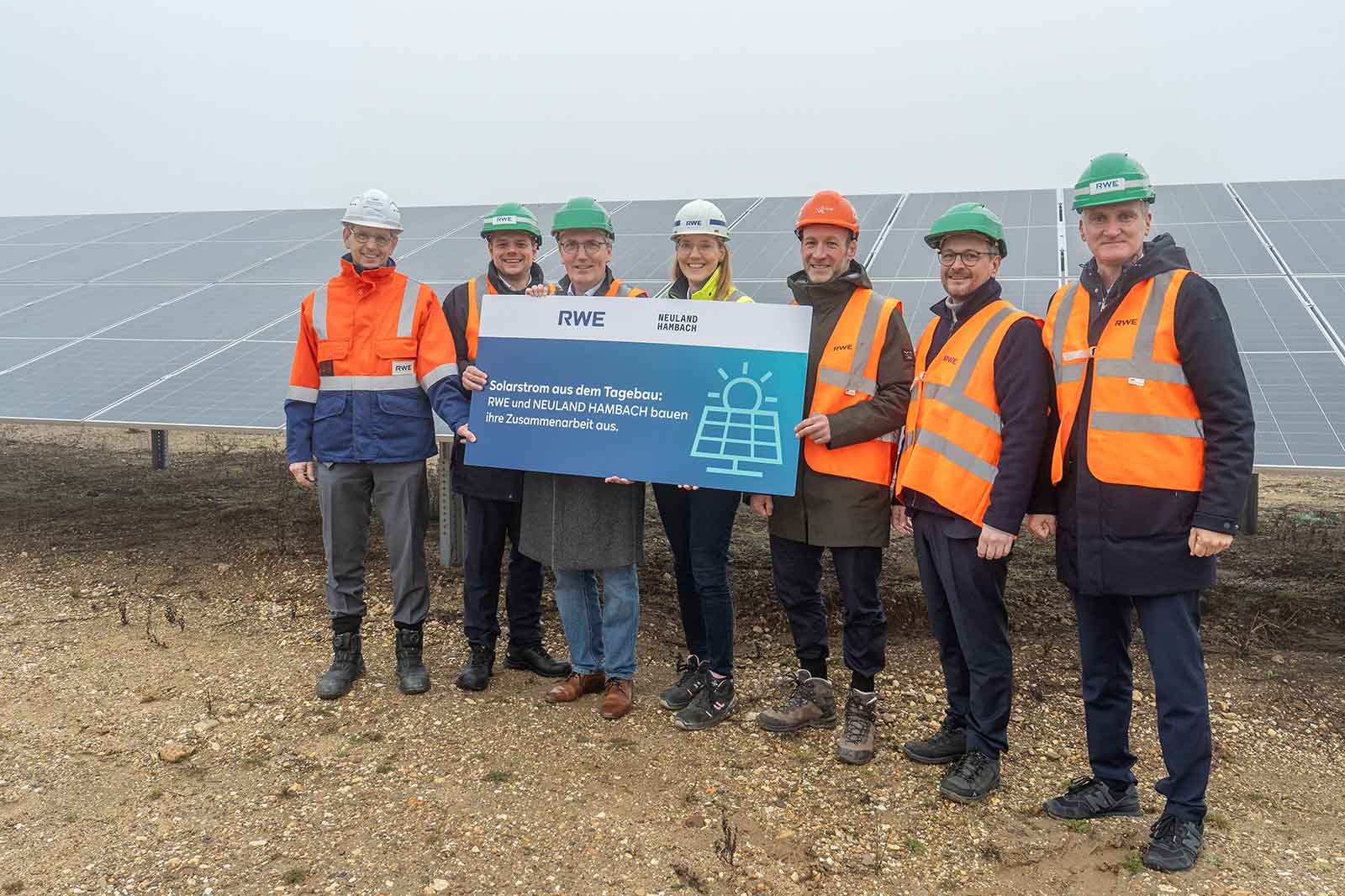 Gruppenfoto von Personen in orangefarbenen Sicherheitswesten vor Solarpanelen mit einem Schild über Solarstrom kooperiert RWE und Neuland Hambach.