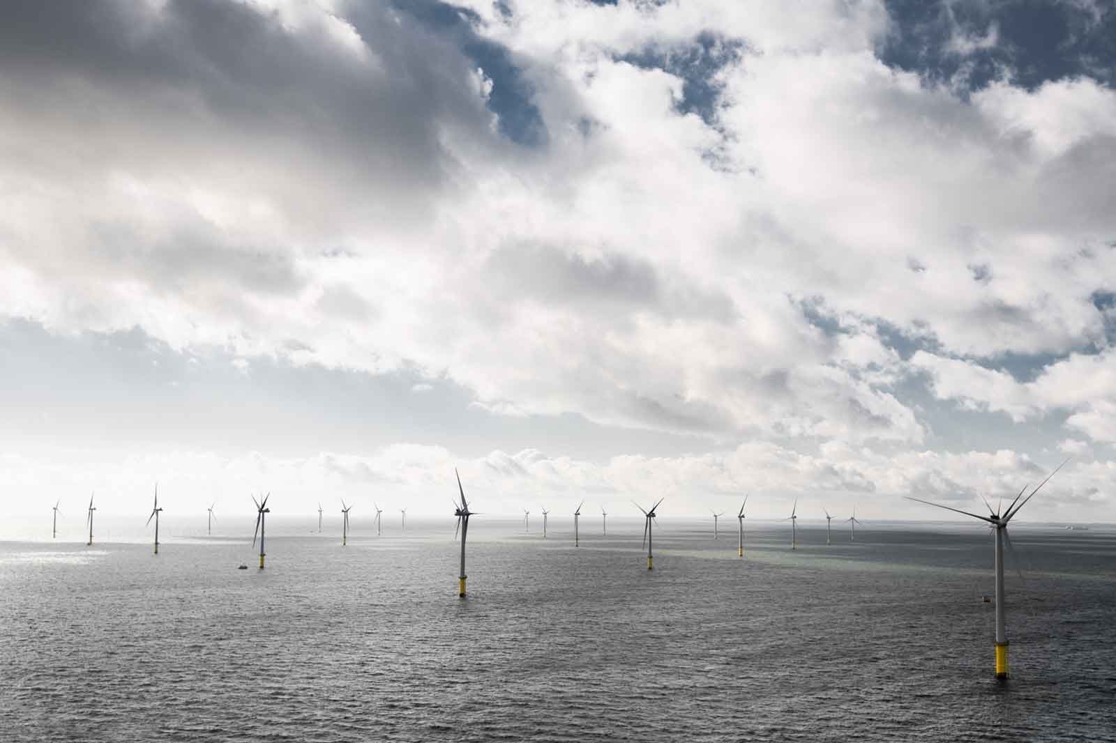 A row of wind turbines stands in the sea under a cloudy sky.