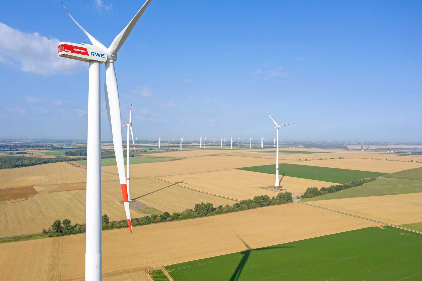 Aerial view of wind turbines in a vast field with green and golden crops.