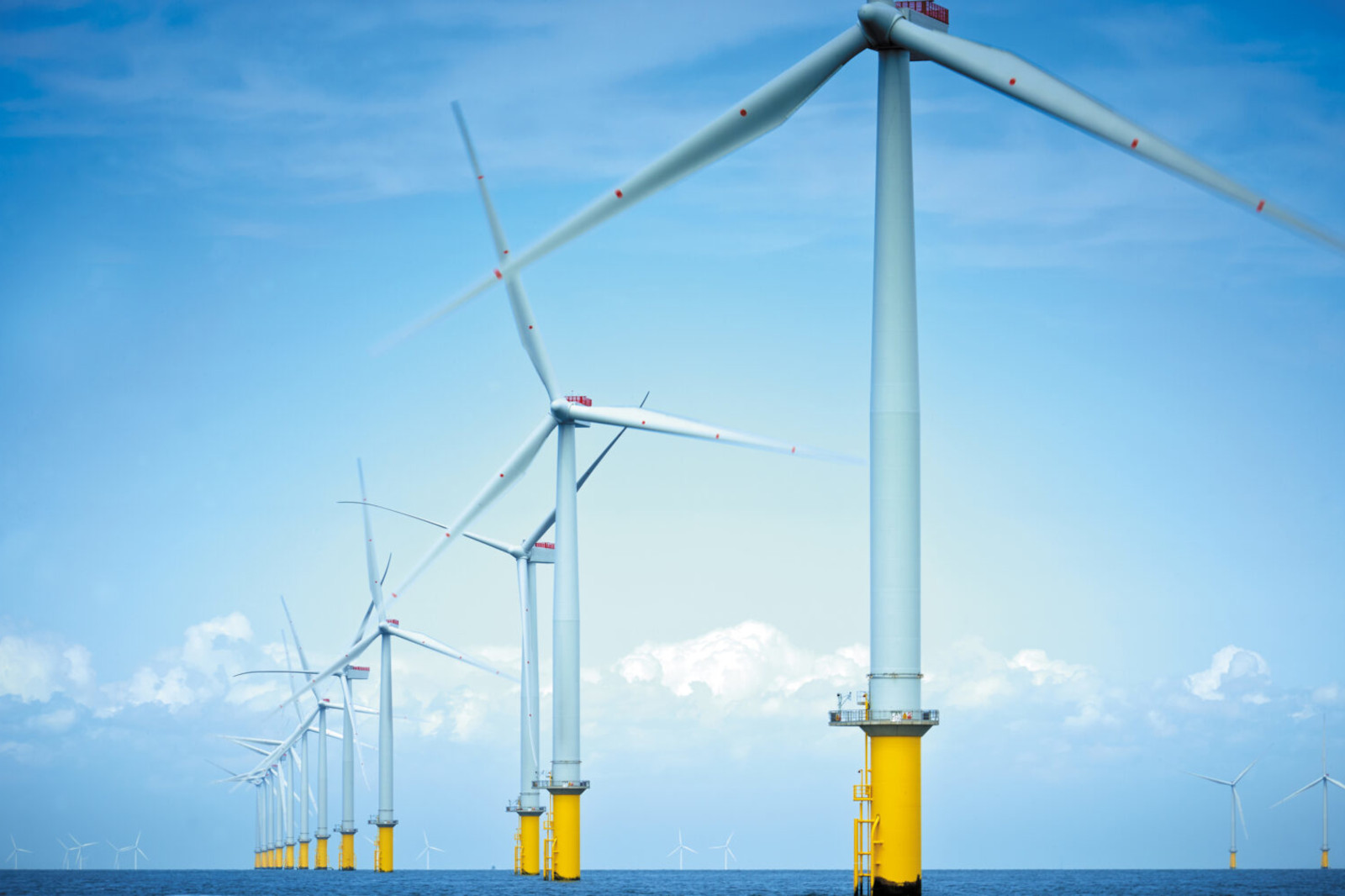 Eine Reihe von Windturbinen steht im Meer, mit gelben Fundamenten und einem klaren blauen Himmel im Hintergrund.