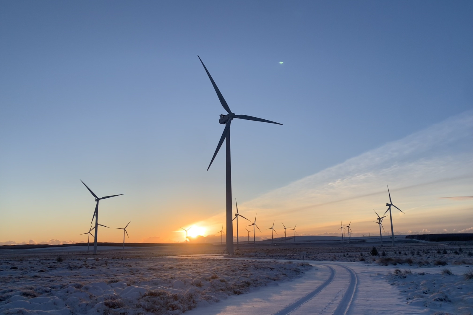 Eine winterliche Landschaft mit Windkraftanlagen, die gegen einen Sonnenuntergang leuchten.
