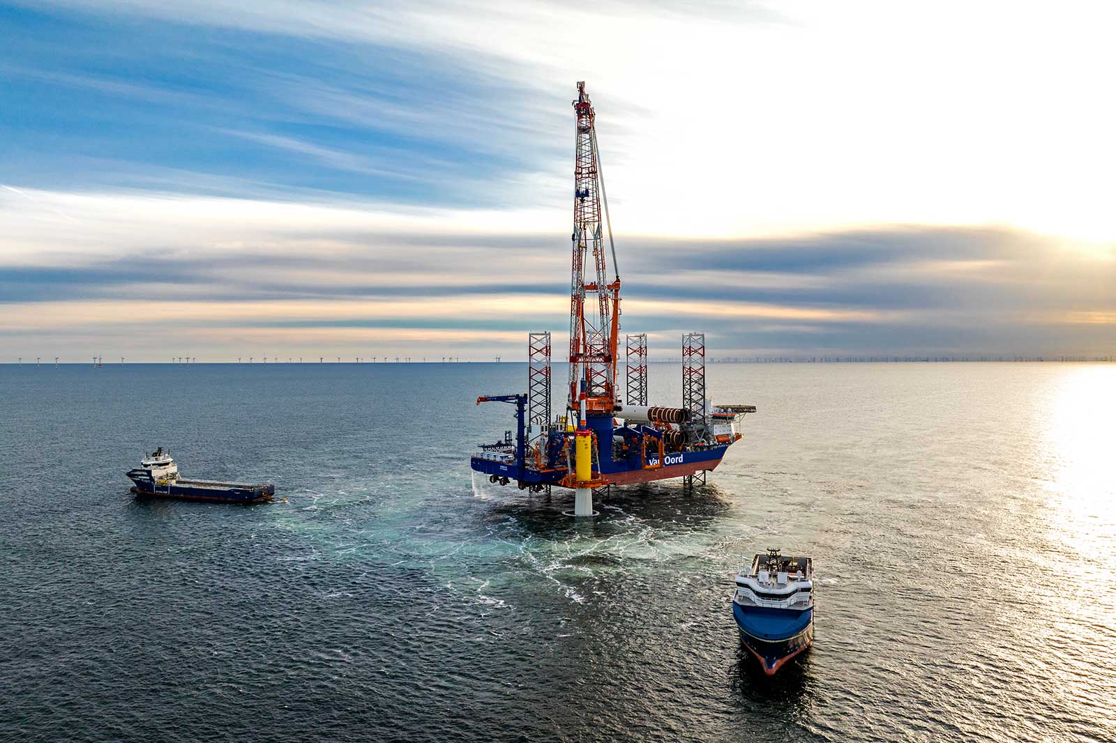 Eine Bohrplattform steht im Meer, umgeben von zwei Schiffen. Der Himmel ist bewölkt und das Wasser reflektiert das Licht.