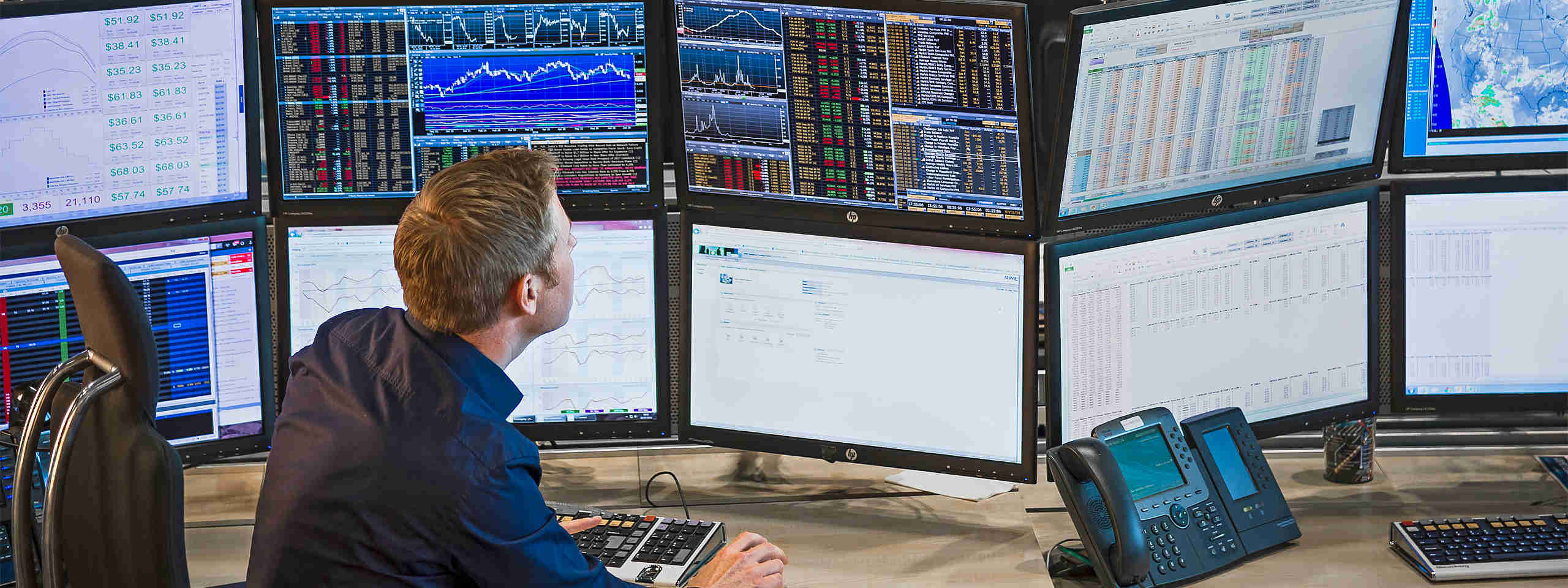Ein Mann sitzt vor mehreren Monitoren, die Finanzdiagramme und Daten anzeigen, während er am Computer arbeitet.