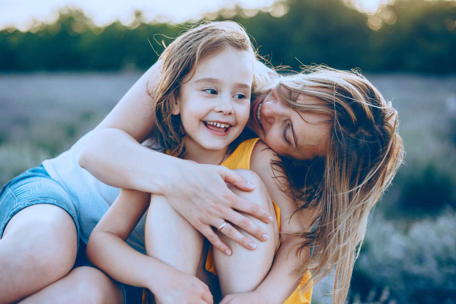 A woman and a child sit closely together in a natural setting, showcasing tenderness and affection.