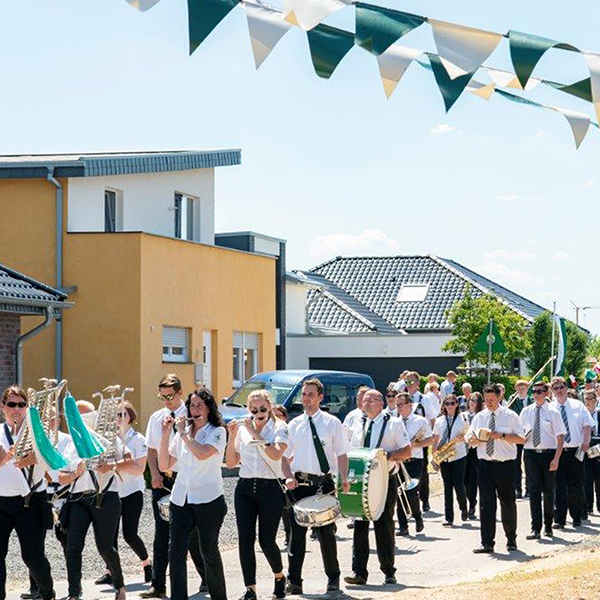 A marching band parades down the street, surrounded by festive flags and modern buildings.