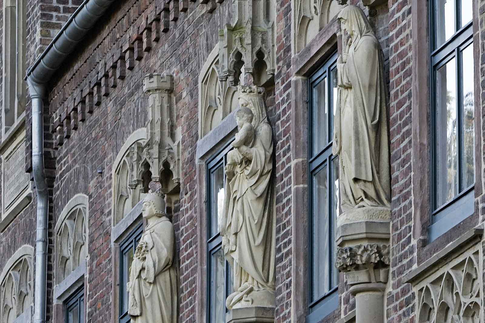 Detaillierte Ansicht einer Backsteinfassade mit kunstvollen Steinskulpturen von Figuren in Nischen.
