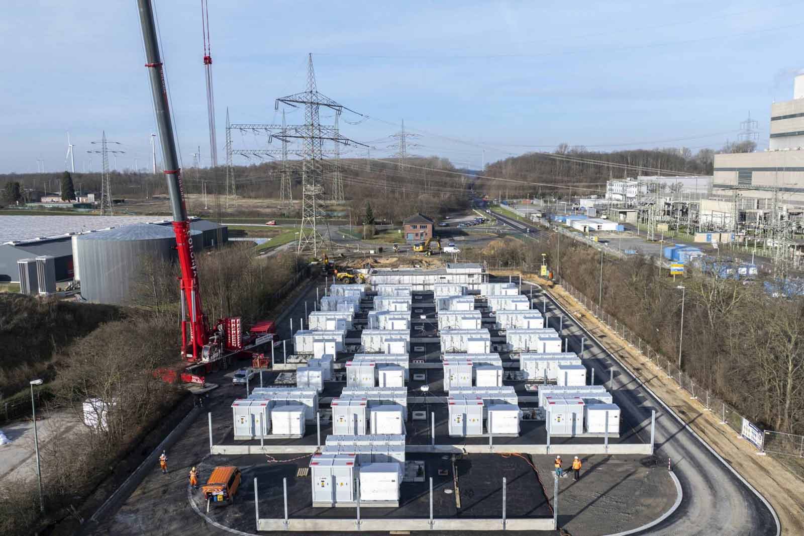 A construction site with many white containers in the foreground, power pylons and an industrial building in the background.