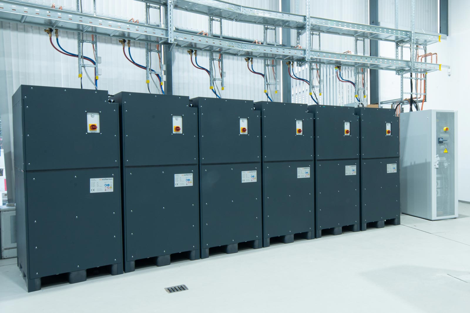 Six large grey energy units are lined up side by side, with a small control unit on the right.
